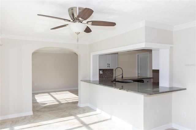 kitchen with arched walkways, ornamental molding, dark stone countertops, a sink, and a peninsula