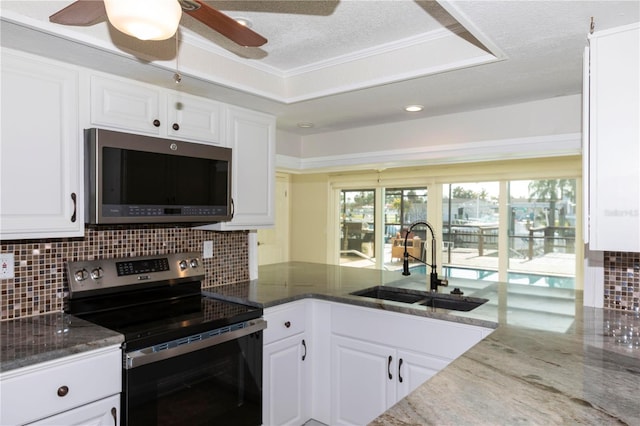 kitchen with stainless steel appliances, a sink, white cabinets, backsplash, and dark stone counters