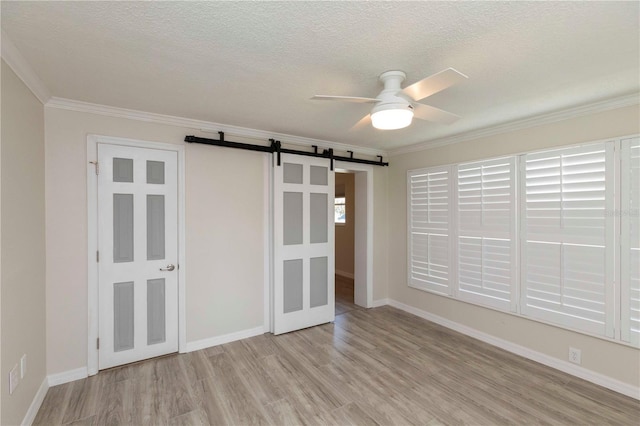 unfurnished bedroom with a barn door, wood finished floors, crown molding, a textured ceiling, and baseboards