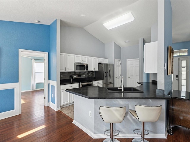 kitchen featuring stainless steel appliances, a sink, dark countertops, a peninsula, and plenty of natural light