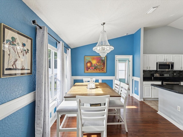dining space featuring lofted ceiling, a chandelier, dark wood-style flooring, and a textured wall