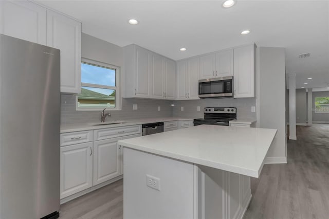 kitchen with stainless steel appliances, a sink, light wood-style floors, light countertops, and a center island