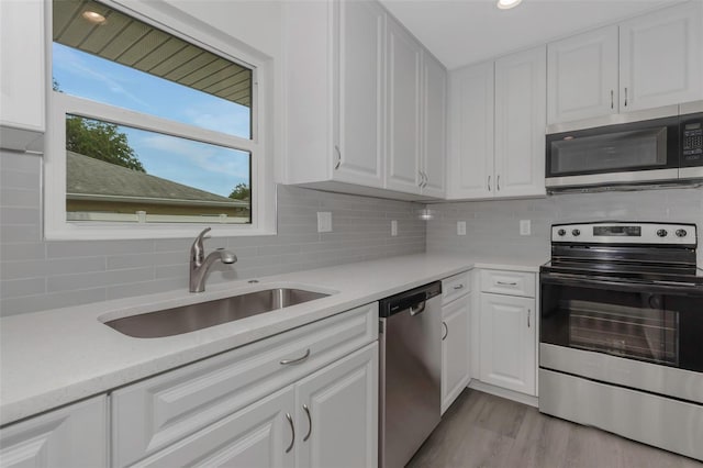 kitchen featuring stainless steel appliances, a sink, light countertops, white cabinetry, and backsplash