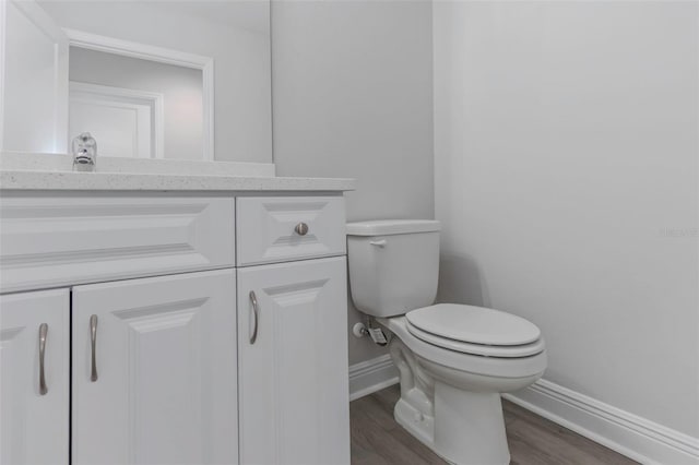bathroom featuring baseboards, toilet, wood finished floors, and vanity