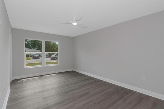 unfurnished room with a ceiling fan, dark wood-type flooring, and baseboards