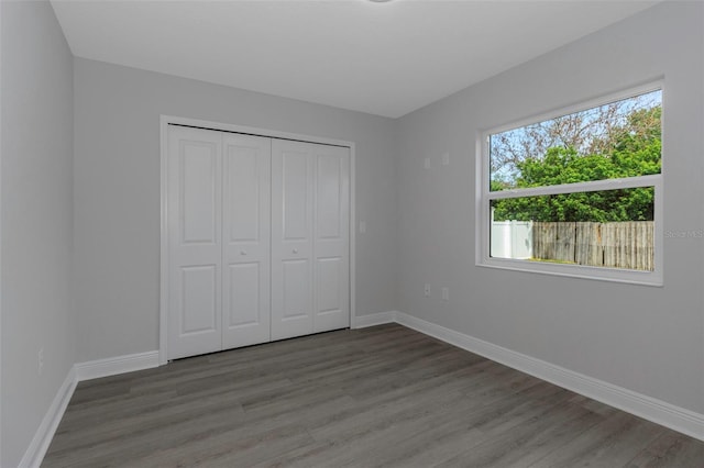 unfurnished bedroom featuring wood finished floors, baseboards, and a closet