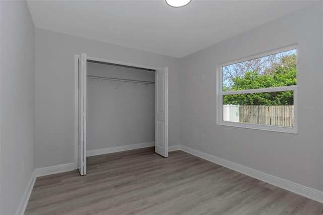 unfurnished bedroom featuring light wood-style flooring, baseboards, and a closet