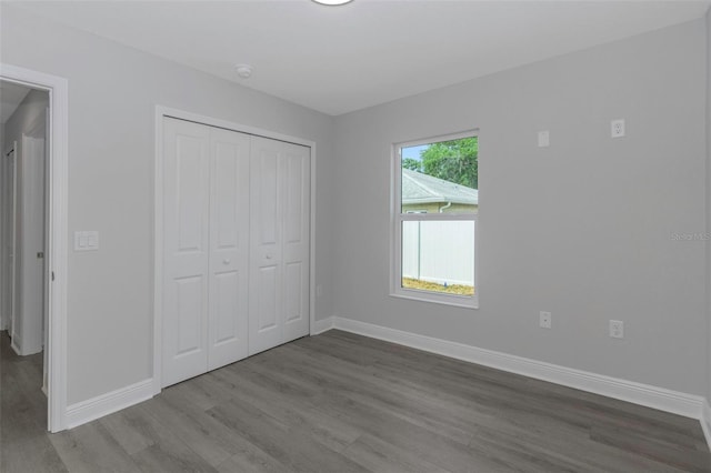 unfurnished bedroom featuring wood finished floors, baseboards, and a closet