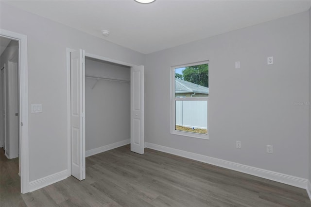 unfurnished bedroom with wood finished floors, baseboards, and a closet