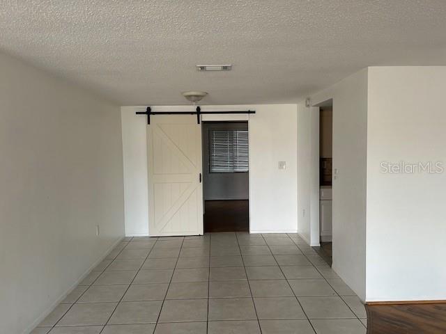 7331 Sandalwood Dr, Port Richey, FL 34668 - hall with a barn door, a textured ceiling, light tile patterned floors, and baseboards