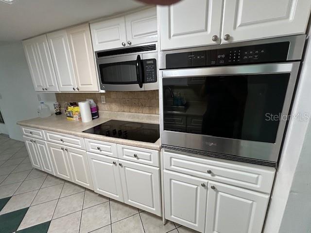 7331 Sandalwood Dr, Port Richey, FL 34668 - kitchen featuring appliances with stainless steel finishes, light tile patterned floors, white cabinets, tasteful backsplash, and light countertops