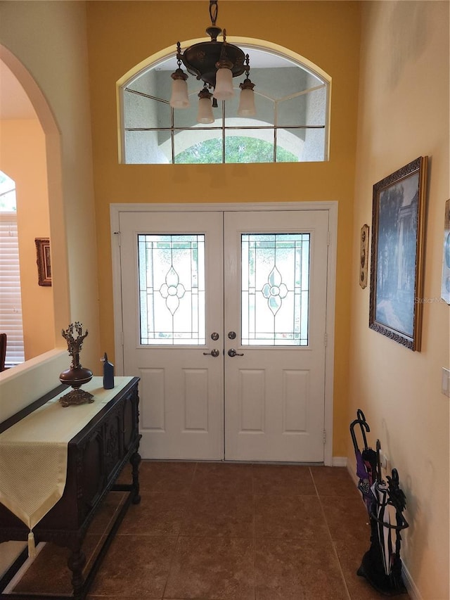 tiled foyer featuring arched walkways, a high ceiling, french doors, baseboards, and a chandelier