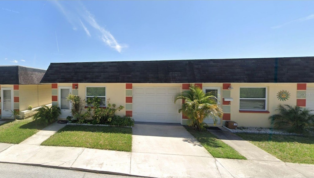 5008 Canner St Unit 4930, New Port Richey, FL 34652 - view of property featuring mansard roof, roof with shingles, concrete driveway, an attached garage, and stucco siding