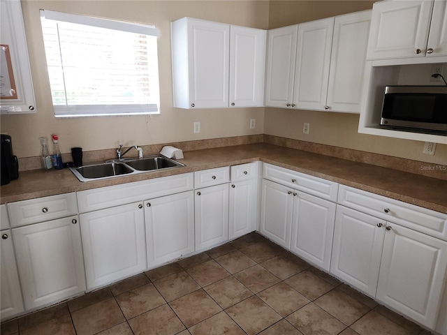 kitchen with a sink, stainless steel microwave, white cabinets, and light tile patterned floors