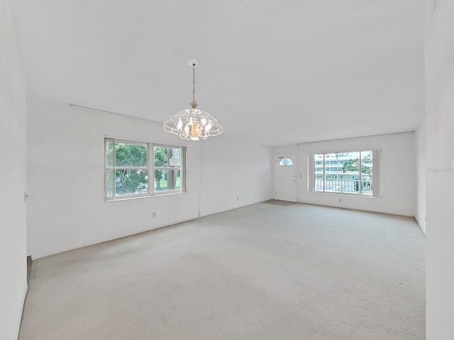 unfurnished room featuring plenty of natural light, a chandelier, and carpet flooring