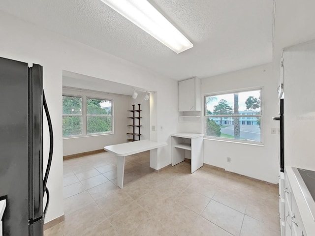 kitchen featuring freestanding refrigerator, white cabinets, light tile patterned floors, a textured ceiling, and light countertops