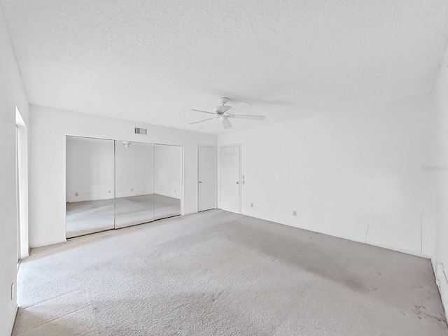 unfurnished bedroom featuring carpet, two closets, a textured ceiling, and a ceiling fan