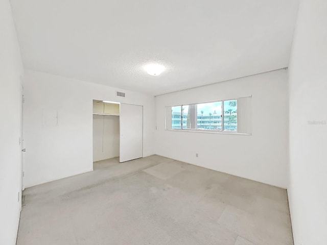 unfurnished bedroom featuring light carpet, a closet, and a textured ceiling