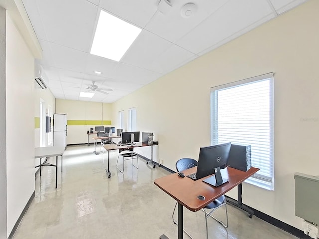 office space featuring a drop ceiling, finished concrete floors, a ceiling fan, baseboards, and plenty of natural light