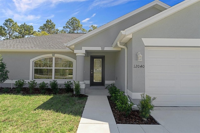 view of exterior entry featuring a garage, a lawn, stucco siding, and roof with shingles