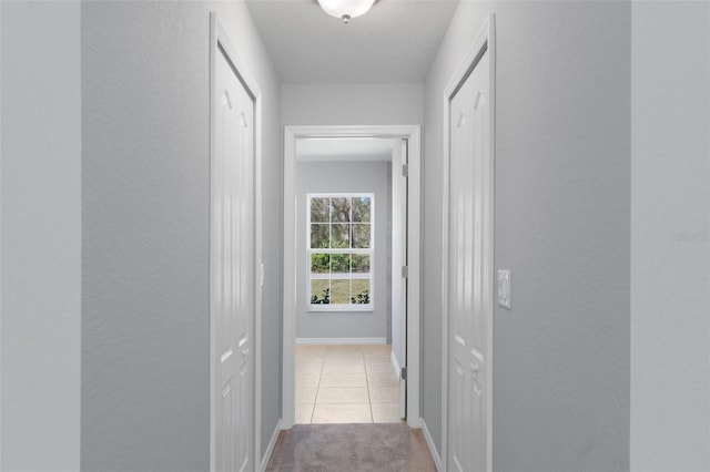 hallway featuring a textured wall, carpet, tile patterned flooring, and baseboards