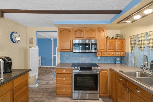 8021 Wildflower Row, Hudson, FL 34667 - kitchen with stainless steel appliances, a sink, decorative backsplash, a textured ceiling, and brown cabinets
