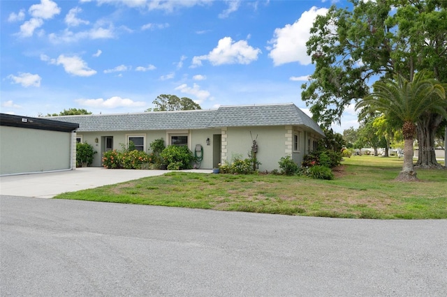 view of front of home featuring concrete driveway, a front lawn, stucco siding, and mansard roof
