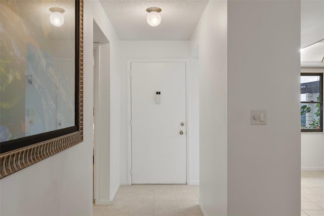 hallway featuring baseboards, light tile patterned floors, and a textured ceiling