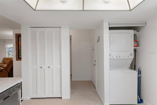 washroom with stacked washing machine and dryer, light tile patterned flooring, and baseboards