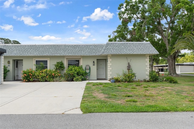 front of property featuring mansard roof, roof with shingles, stucco siding, and a front yard