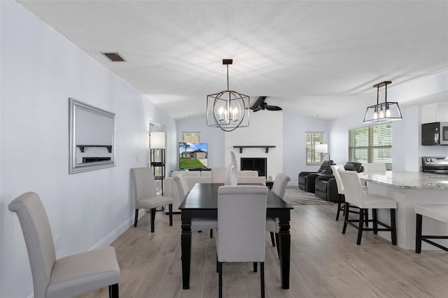 7520 Mako Dr, Hudson, FL 34667 - dining space with a chandelier, light wood finished floors, vaulted ceiling, baseboards, and a fireplace
