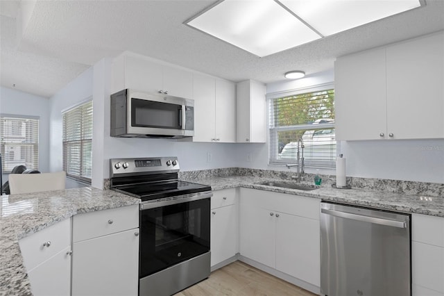 7520 Mako Dr, Hudson, FL 34667 - kitchen featuring stainless steel appliances, a sink, light wood-style flooring, a textured ceiling, and white cabinetry