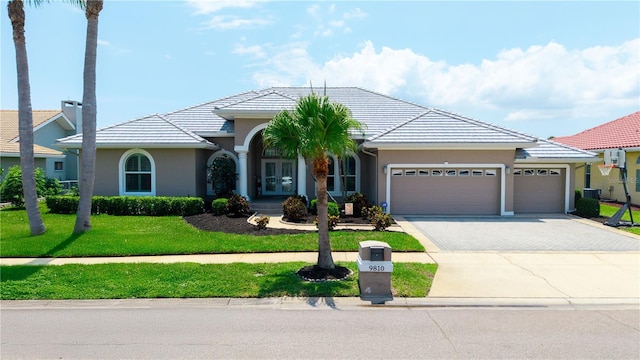 view of front facade featuring french doors, driveway, an attached garage, stucco siding, and a front yard