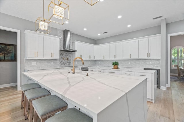 kitchen featuring wall chimney range hood, light wood finished floors, decorative backsplash, a spacious island, and white cabinets