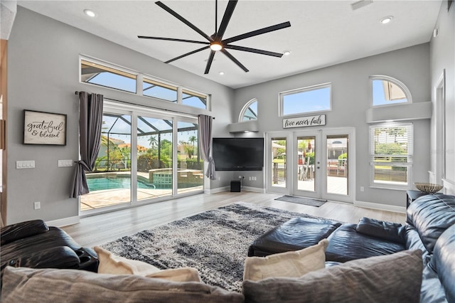 living area with ceiling fan, plenty of natural light, wood finished floors, a high ceiling, and recessed lighting