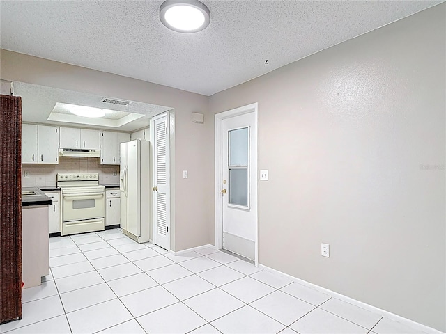 13003 Sandburst Ln, Hudson, FL 34667 - kitchen with white appliances, under cabinet range hood, dark countertops, light tile patterned flooring, and a textured ceiling