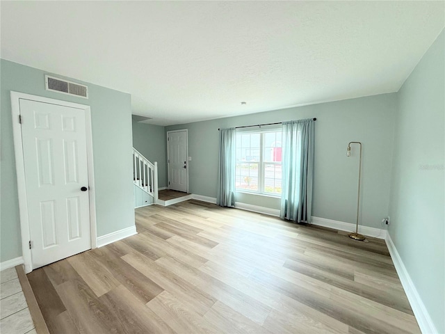 unfurnished living room with stairway, light wood-type flooring, and baseboards