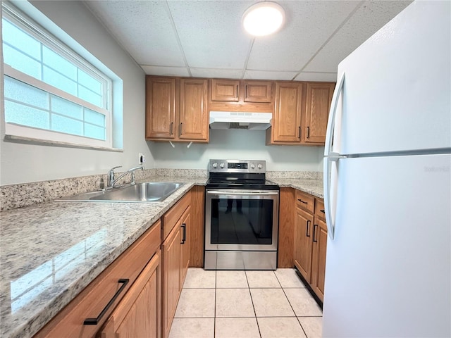 kitchen with freestanding refrigerator, stainless steel electric range oven, under cabinet range hood, a sink, and a paneled ceiling