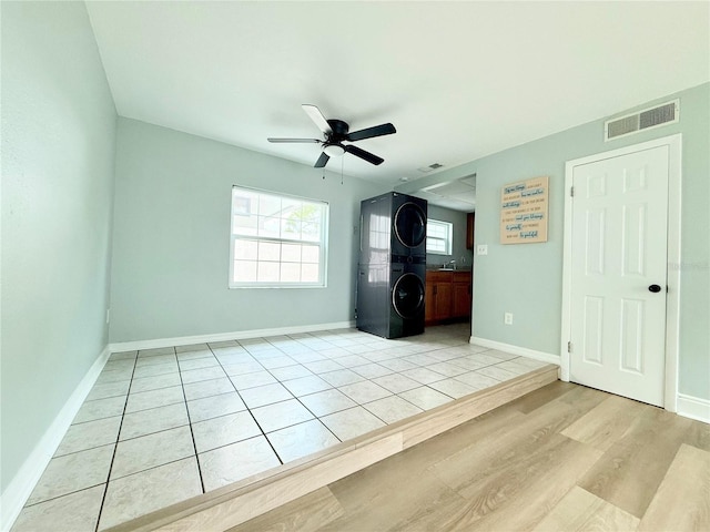 unfurnished bedroom with stacked washer and clothes dryer, baseboards, a ceiling fan, and light wood-type flooring