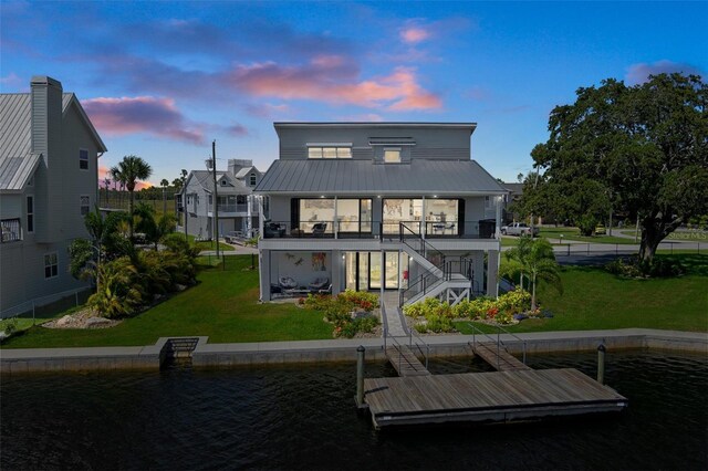back of house at dusk featuring stairway, a lawn, metal roof, and a water view