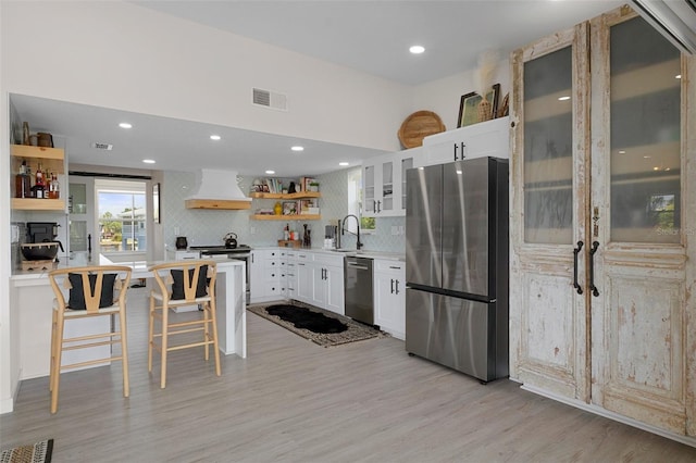 kitchen featuring stainless steel appliances, open shelves, premium range hood, decorative backsplash, and white cabinets