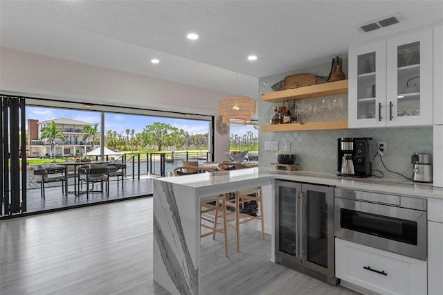 bar area with beverage cooler, light wood-type flooring, recessed lighting, decorative backsplash, and stainless steel oven
