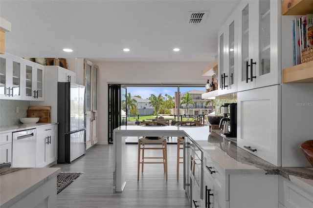 kitchen featuring freestanding refrigerator, dishwashing machine, light wood-type flooring, backsplash, and white cabinetry