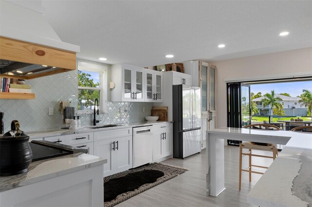 kitchen with freestanding refrigerator, dishwasher, a sink, premium range hood, and light wood-type flooring