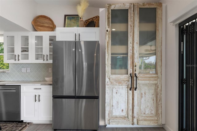 kitchen with appliances with stainless steel finishes, glass insert cabinets, light countertops, backsplash, and white cabinetry