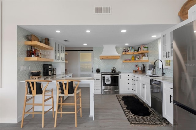 kitchen featuring open shelves, custom range hood, stainless steel appliances, backsplash, and white cabinets