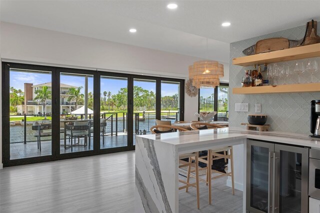 kitchen with wine cooler, backsplash, recessed lighting, light wood finished floors, and a water view