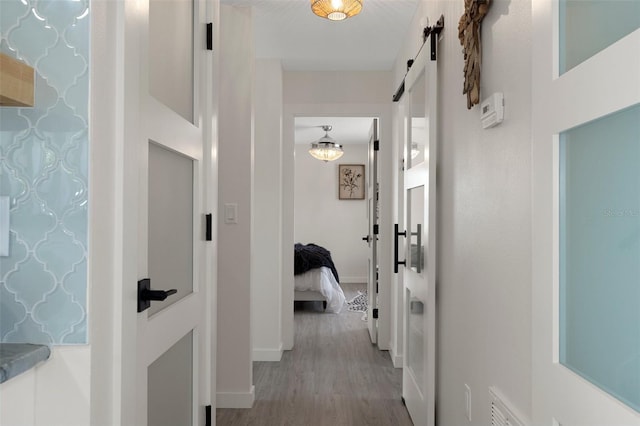 hallway featuring a barn door, wood finished floors, and baseboards
