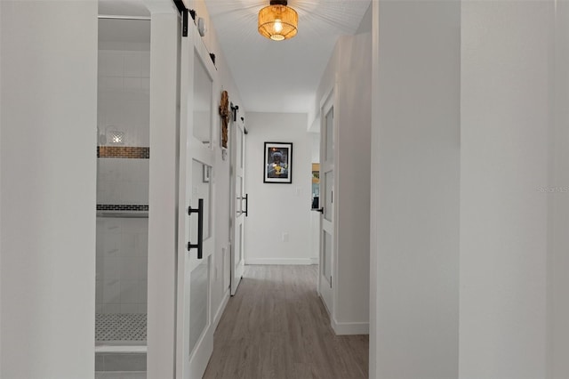 hall featuring a barn door, baseboards, and wood finished floors