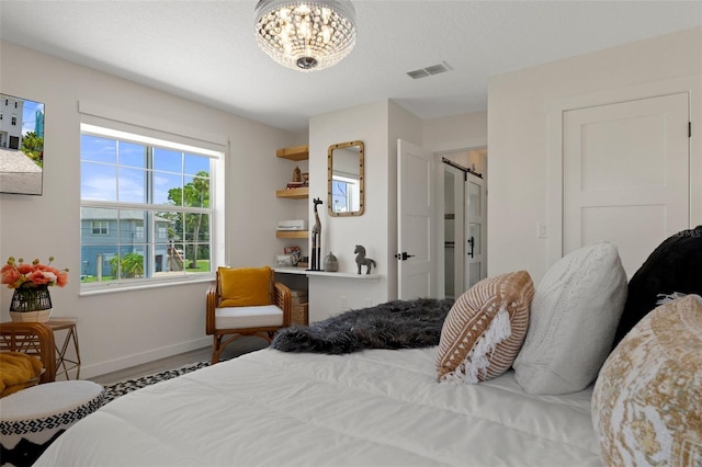 bedroom featuring wood finished floors, baseboards, a chandelier, and a barn door